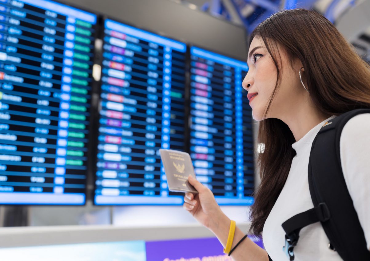 woman-holding-her-passport-with-flight-information-board-international-airport-scaled